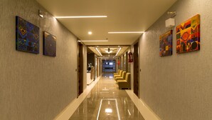 A modern hotel corridor with a polished floor, artwork on the walls, and a reception desk at the end. - Hotel Green City (Gandhinagar)