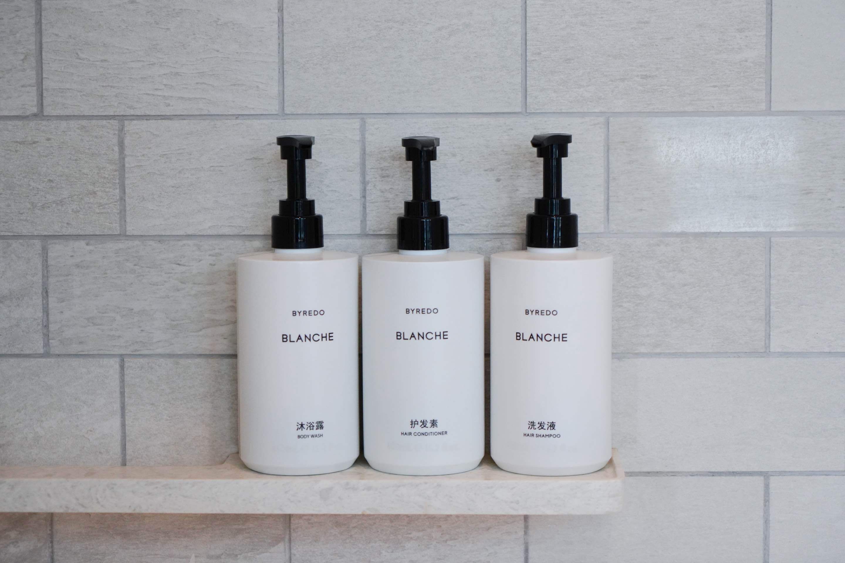 Three white bottles with black pumps on a shelf against a tiled wall.