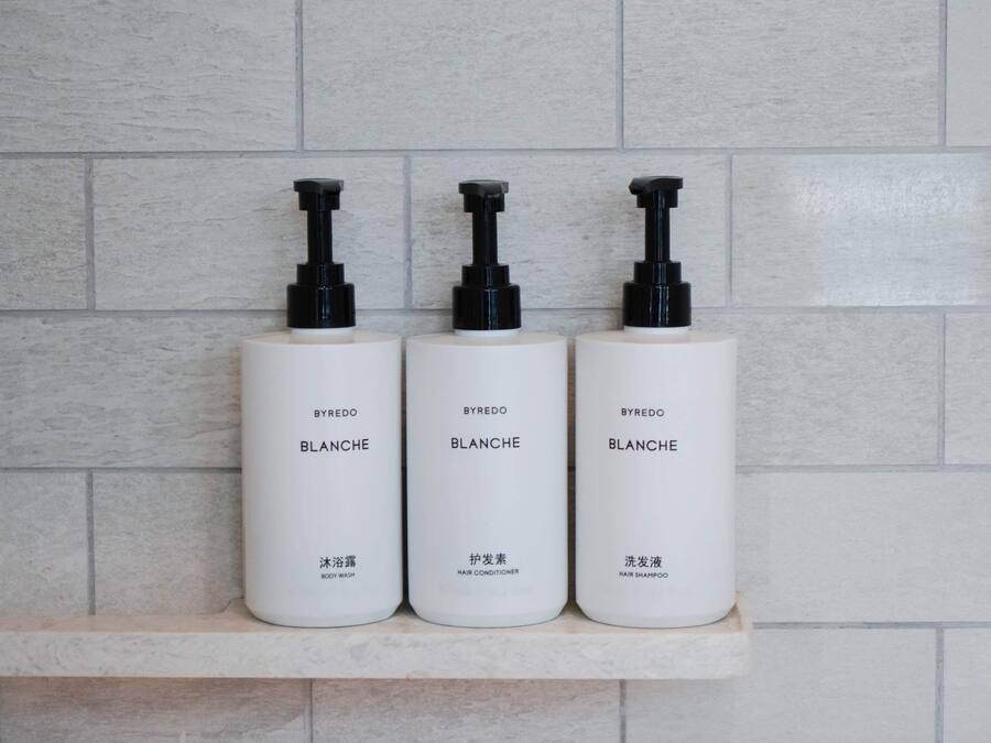 Three white bottles with black pumps on a shelf against a tiled wall.