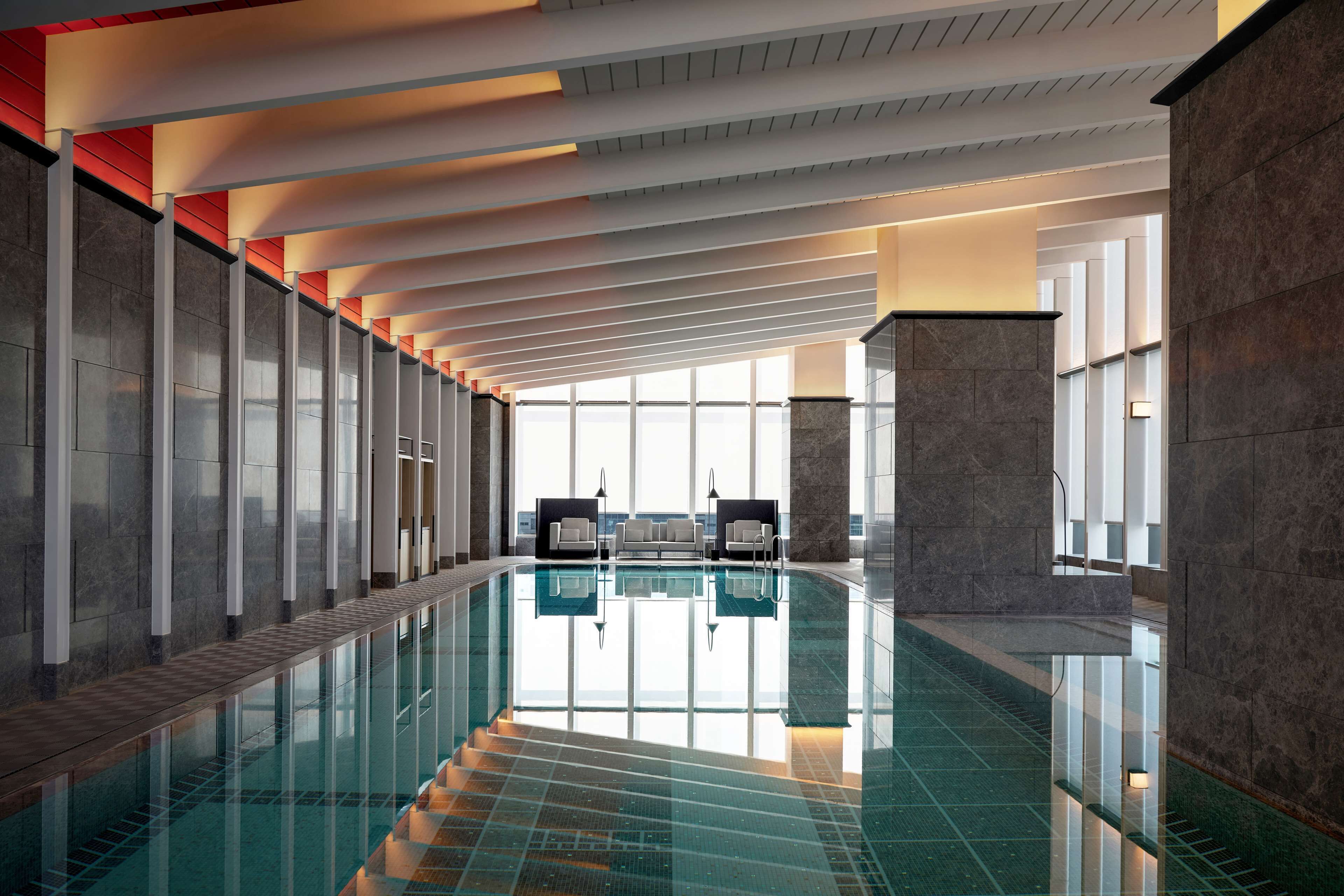 Ein moderner, überdachter Pool mit großer, spiegelnder Fläche, Panoramafenstern und minimalistischer Gestaltung.