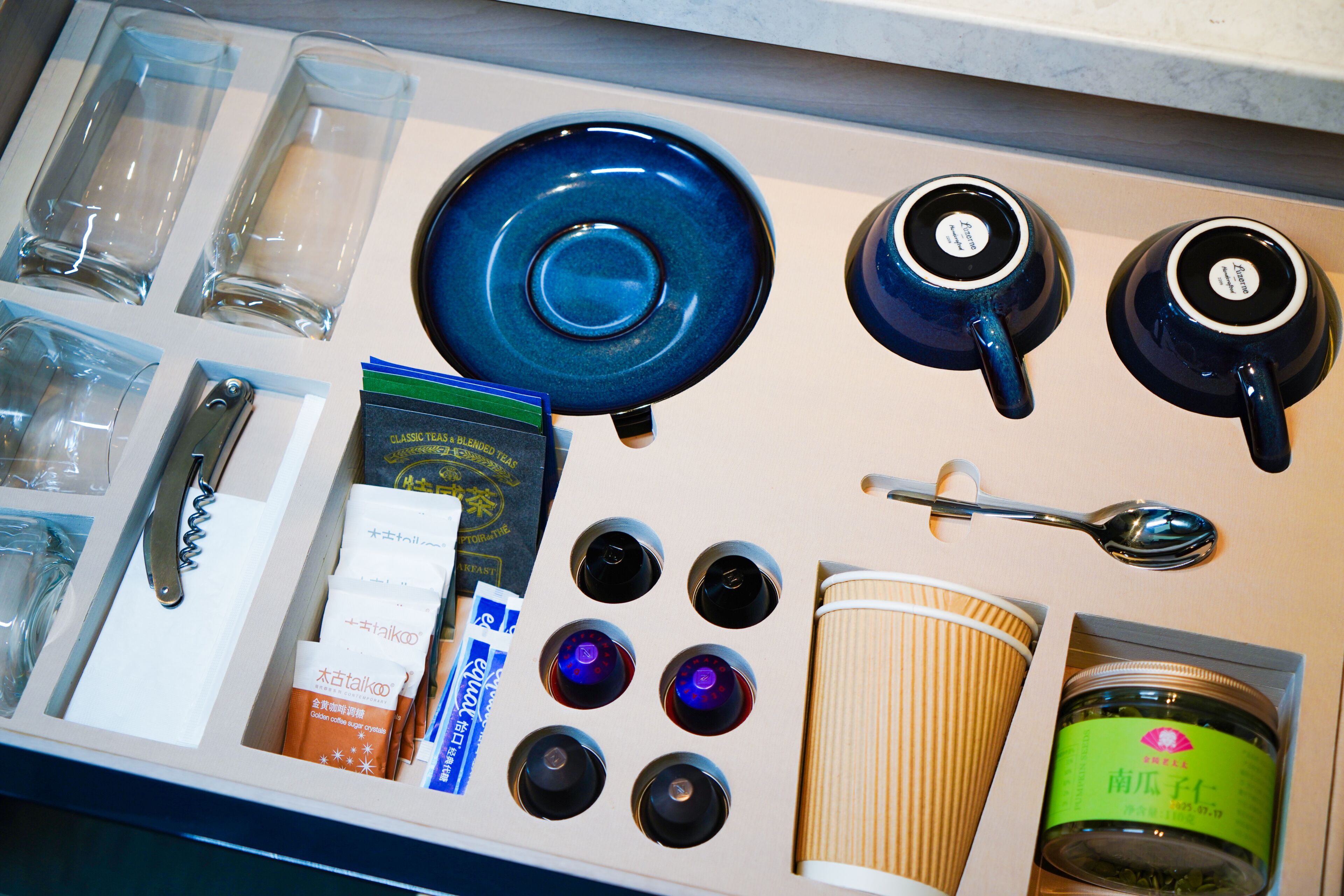 A kitchen counter with various items including glasses, plates, a spoon, a coffee cup, and packaged goods.