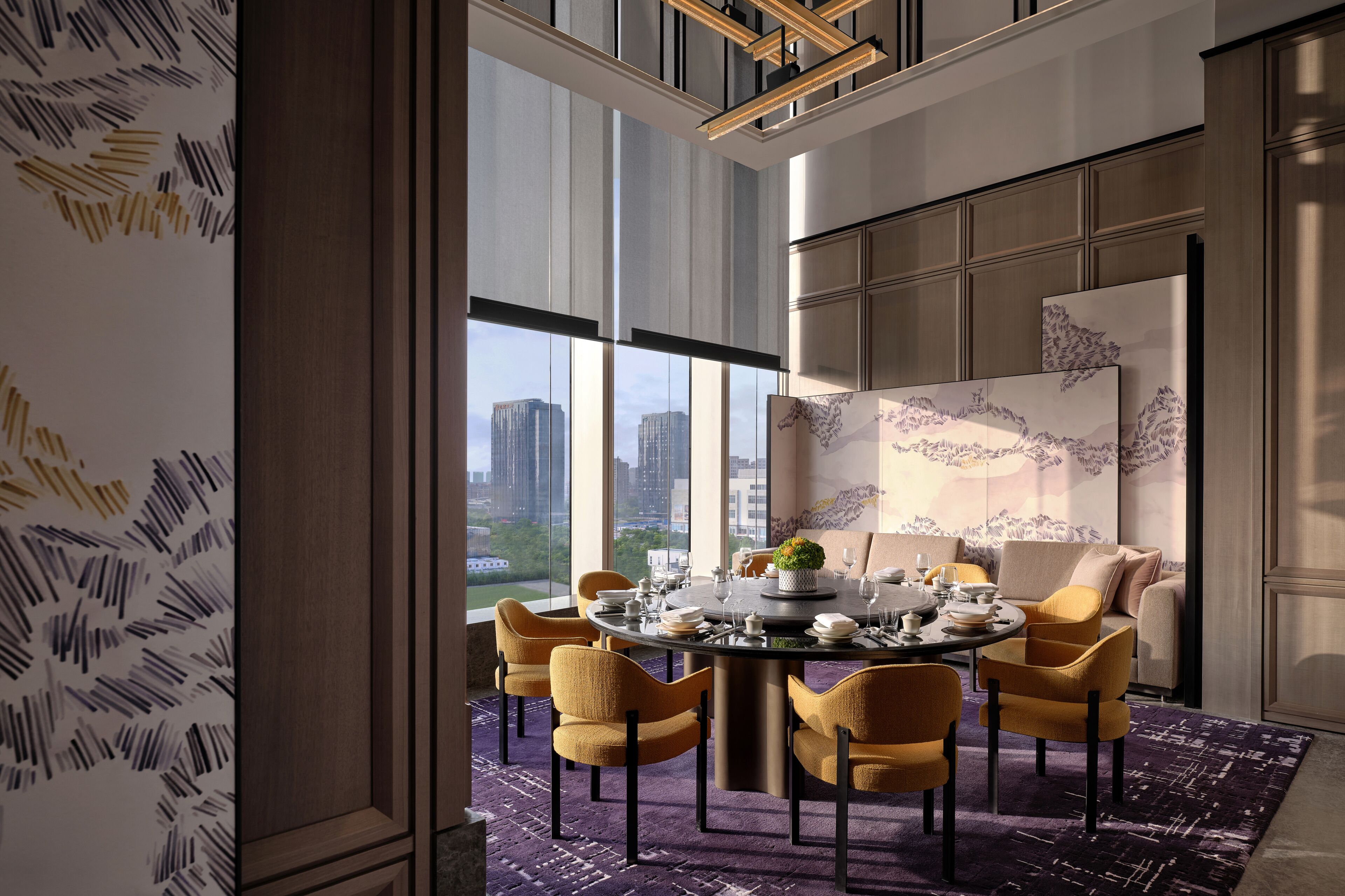 A modern dining area with a round table, yellow chairs, and a city view through large windows.