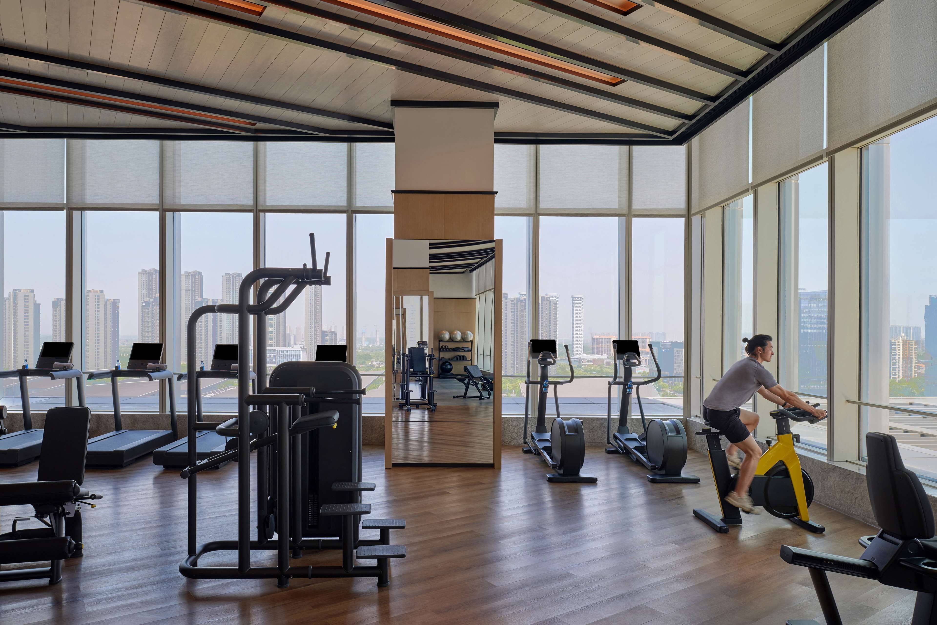 A spacious gym with large windows, exercise equipment, and a city view.