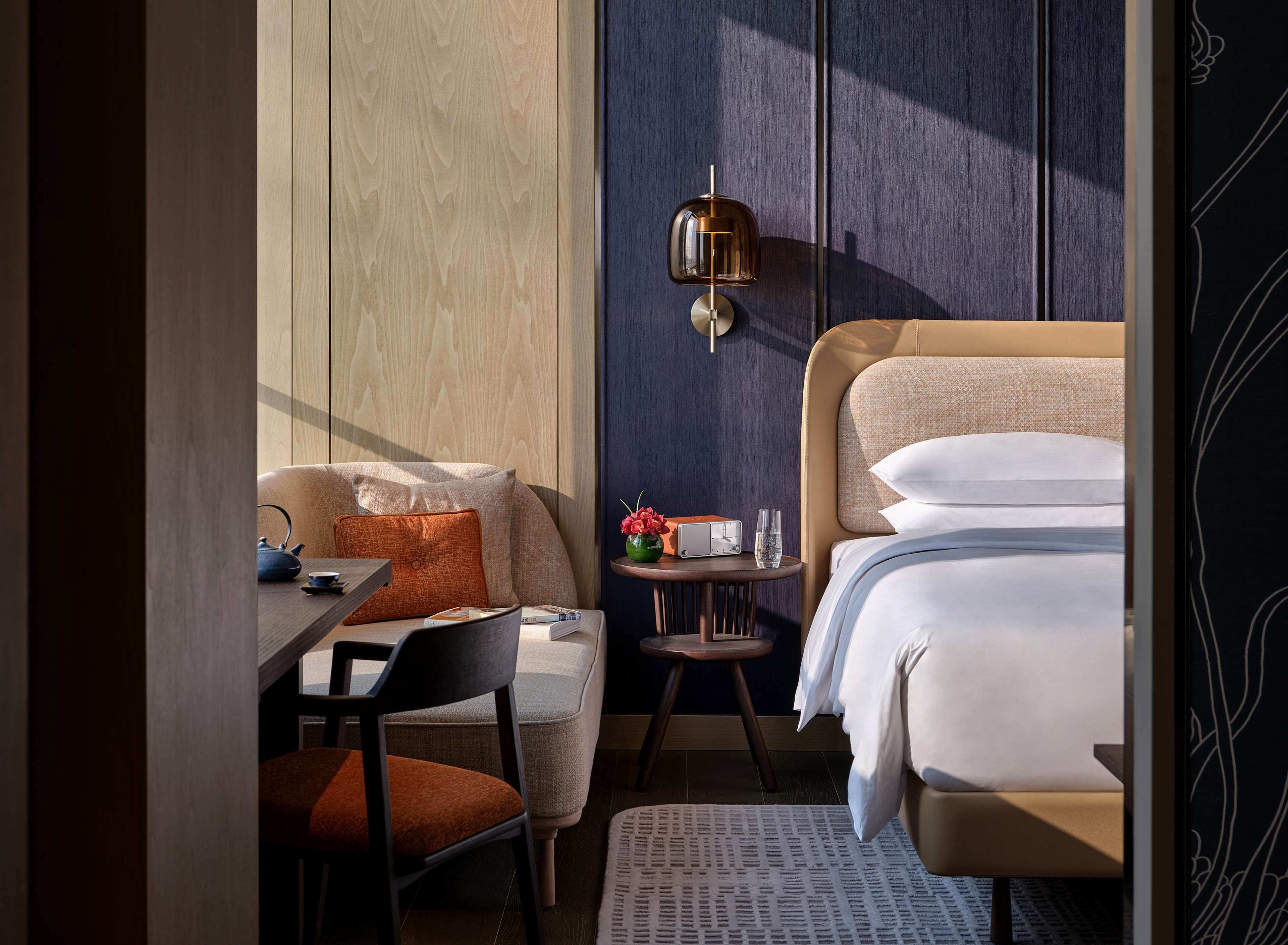 Habitació d'hotel moderna amb un llit, escriptori, cadira i taula petita amb un ram i un aparell de ràdio.