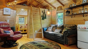 Un interior de cabaña acogedor con un sillón de cuero, un sofá de cuero negro, una mesa de comedor de madera y un refrigerador.