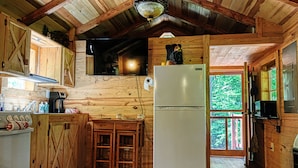 Cocina de cabaña de madera con refrigerador, armarios de madera, microondas y televisor.
