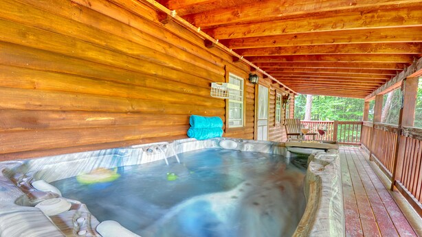 Una cabaña de madera con jacuzzi y terraza techada.