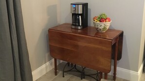 Una mesita de madera con una cafetera y un cuenco de fruta.