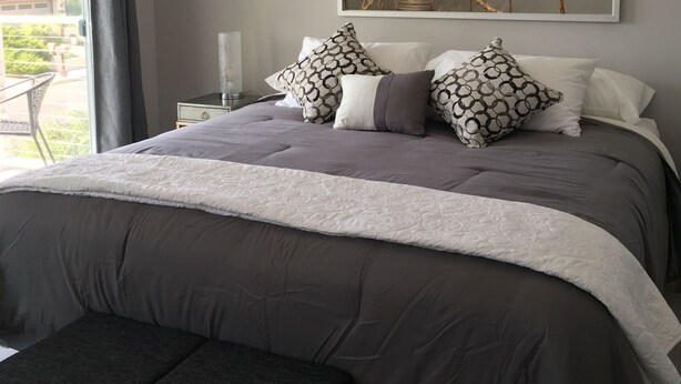 Un dormitorio con una cama grande, ropa de cama gris y un cuadro grande con una imagen de un puente colgante.