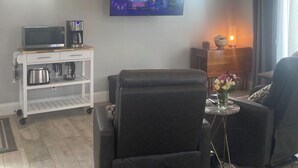 Una sala de estar con televisión de pantalla plana, ventilador de techo, cafetera, microondas y una pequeña mesa con un jarrón de flores.