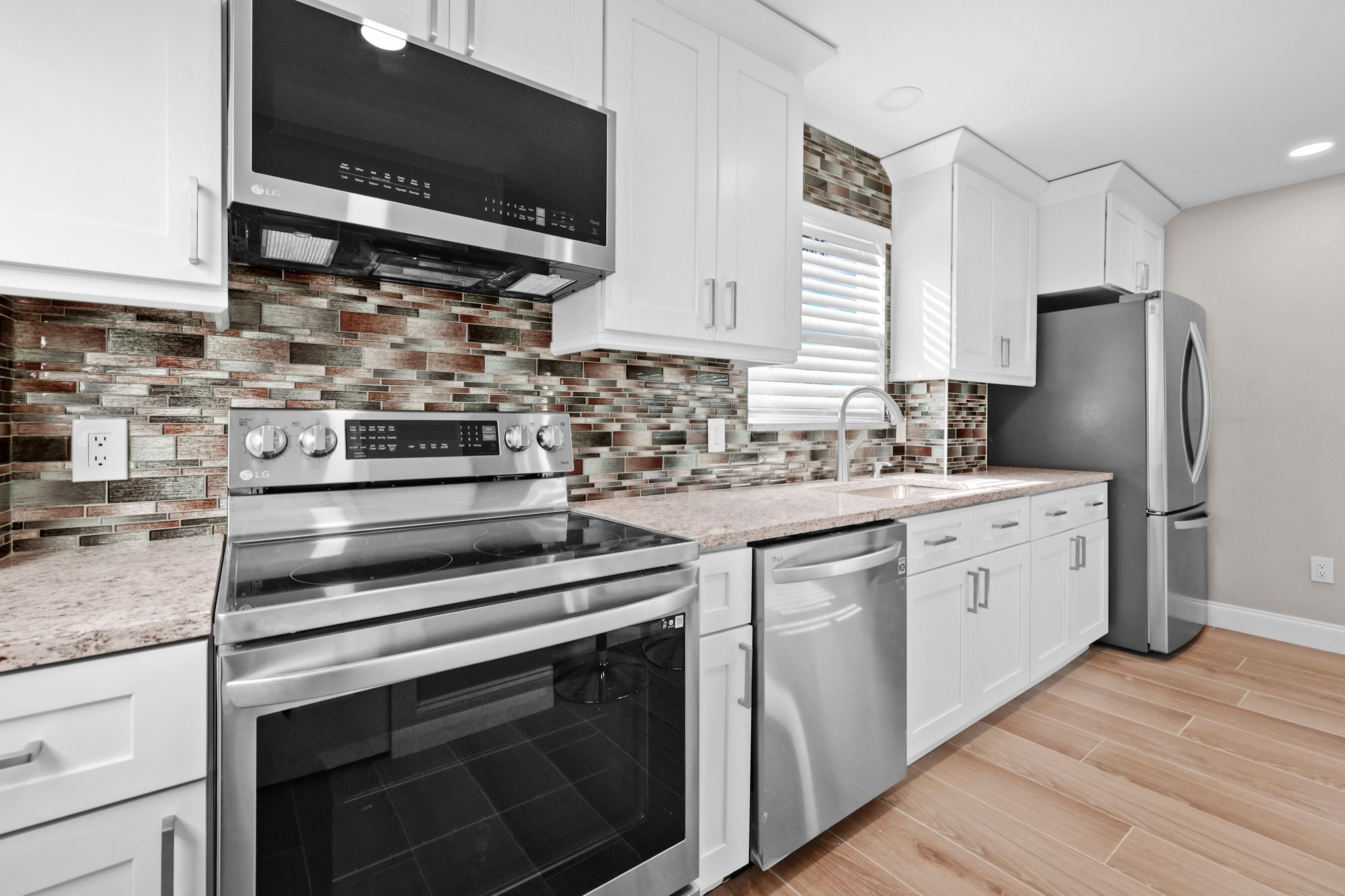 A modern kitchen with stainless steel appliances, white cabinetry, and a patterned backsplash.