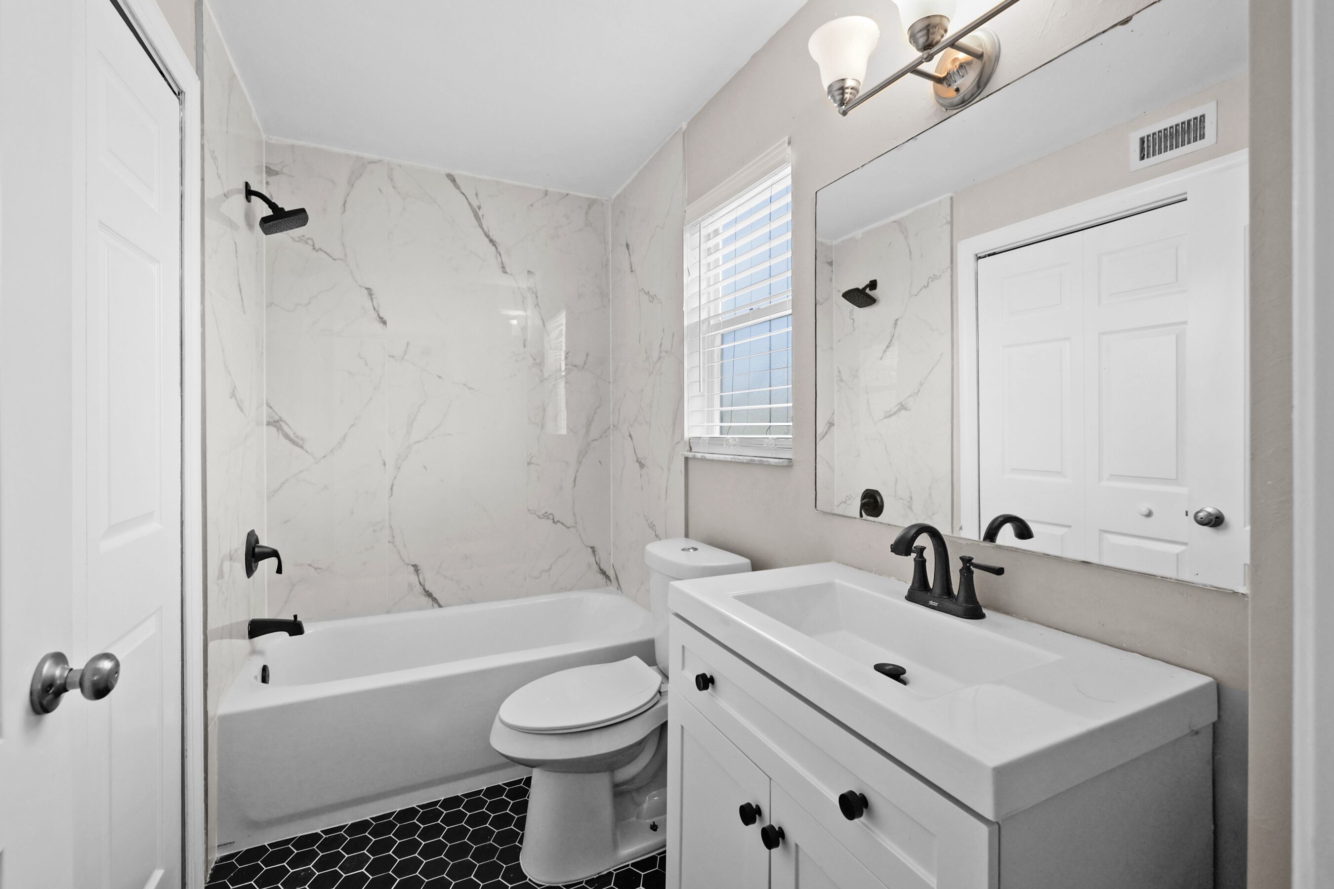 A modern bathroom with a white bathtub, toilet, and sink, marble walls, and a large mirror.