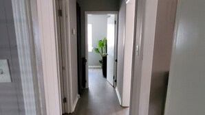 Ein Flur mit weißen Wänden und Türen, der in einen Raum mit einer Pflanze führt.