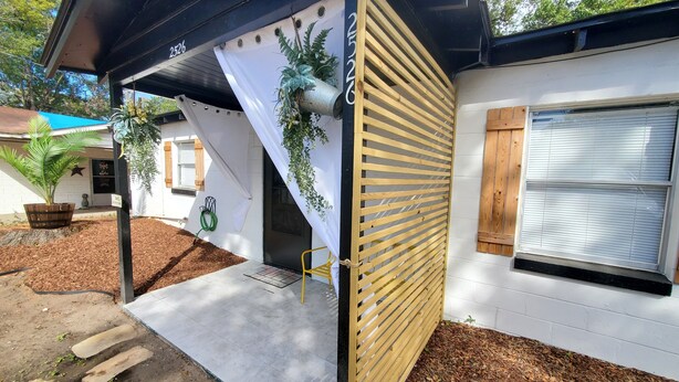 Ein Haus mit einer überdachten Veranda, einem Holzzaun und einem Blumentopf.