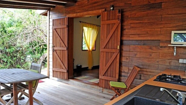 Un rustico chalet in legno con tavolo e sedie, angolo cottura con stufa e un'ampia porta aperta su una stanza con tenda gialla.