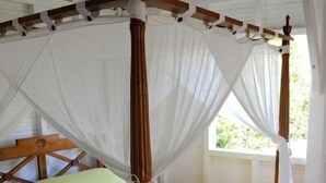 Un letto a baldacchino con struttura in legno e tende bianche, posato su un pavimento piastrellato con un tappeto decorato.