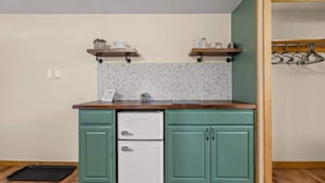 A compact kitchen with teal cabinets, a white refrigerator, and wooden shelves above the countertop. - Cozy Poconos Cabin in the Pines | Firepit & Pickle (Barrett Township)
