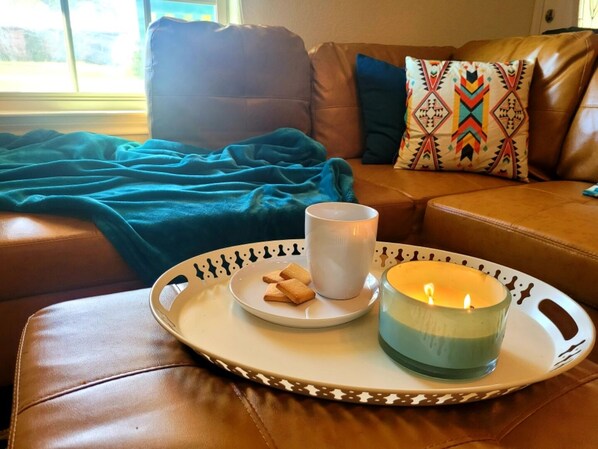 A tray with a candle, a mug, and cookies on a leather couch.