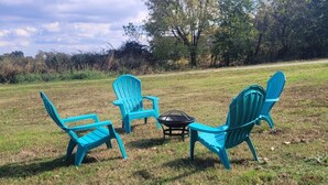 Neljä turkoosinsinistä Adirondack-tyylistä tuolia on asetettu riviin ruohikkoiselle alueelle, ja niiden keskellä on musta pöytä.