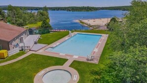 Une piscine avec un jacuzzi circulaire, entourée d’une pelouse et d’un bâtiment.
