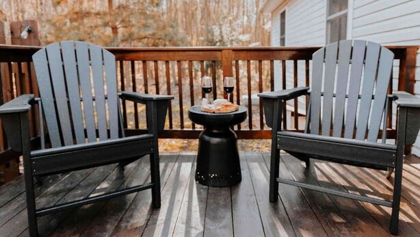 Une terrasse en bois avec deux fauteuils Adirondack et une petite table ronde sur laquelle se trouvent une pizza et deux verres de vin.