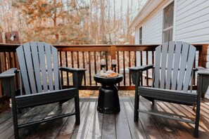 A wooden deck with two Adirondack chairs and a small round table with a pizza and two glasses of wine.