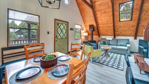 A spacious loft-style living area with a high ceiling, wooden beams, and large windows offering views of the outdoors. - Deck & Grill: A-Frame Cabin in Munds Park! (Munds Park)