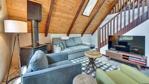 A cozy loft-style living room with a wooden ceiling, a large TV, and a sofa. - Deck & Grill: A-Frame Cabin in Munds Park! (Munds Park)