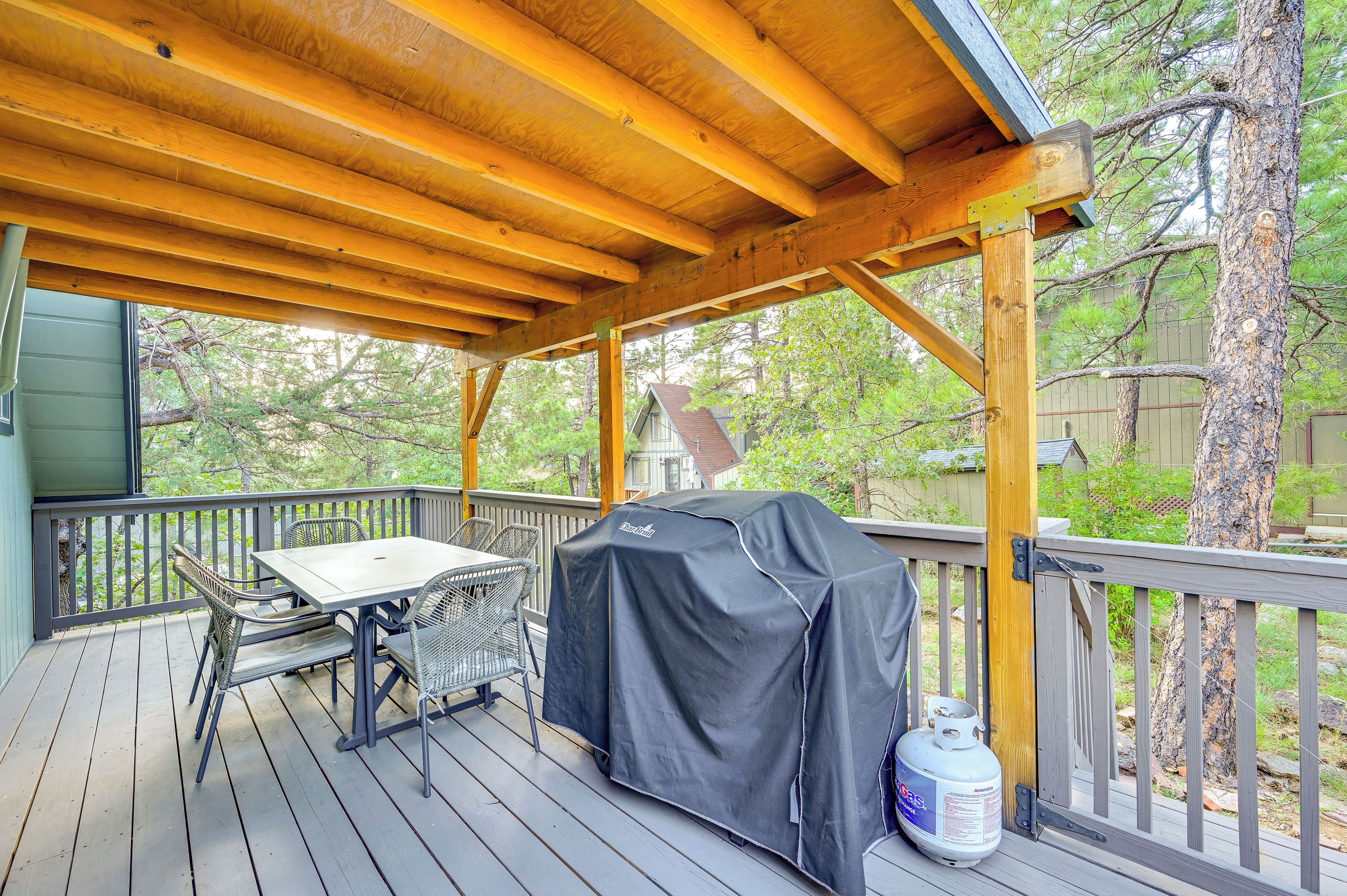 A covered outdoor deck with a grill, table, chairs, and a propane tank.