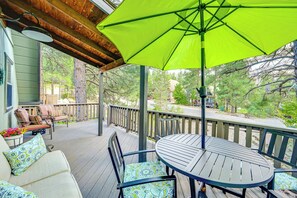 Een overdekt terras buiten, met een tafel en stoelen, een felgroene parasol, en zicht op bomen en een huis op de achtergrond.