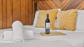 A neatly made bed with a bottle of wine and a glass, a rolled towel, and two pillows. - Cozy & Chic Pocono Cabin | Firepits | Pickleball (Barrett Township)