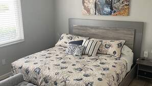 A bedroom with a bed, a ceiling fan, a window with blinds, and a wall with three paintings. - Fully remodeled 1/1 apartment (Marco Island)