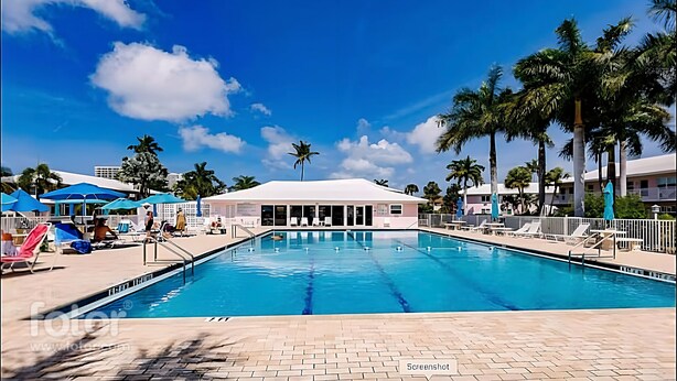 A swimming pool with lounge chairs and umbrellas, surrounded by palm trees and a building with a white roof. - Fully remodeled 1/1 apartment (Marco Island)