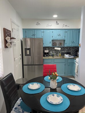 A compact kitchen with teal cabinets, a stainless steel refrigerator, and a red chair.