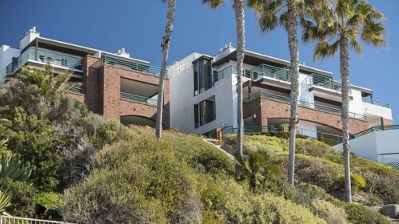Un edificio moderno de varios pisos con balcones, rodeado de exuberante vegetación y palmeras.