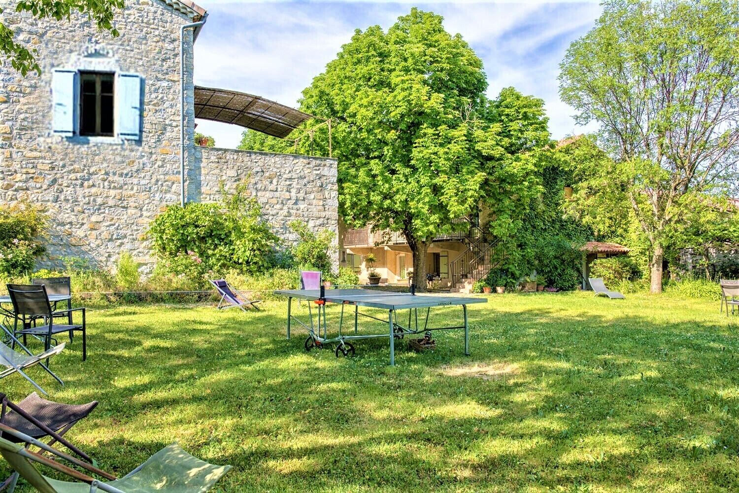 A stone building with a tennis court, outdoor seating, and a large tree.