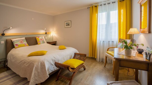 Una habitación de hotel con una cama, un escritorio, una silla y un ventanal con cortinas amarillas.