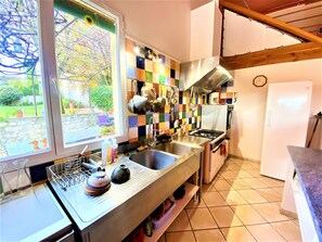 A kitchen with a large window, a tiled backsplash, stainless steel appliances, and a wooden ceiling.