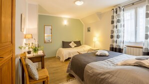 Habitación de hotel con dos camas, un armario de madera, una mesita de noche con lámpara, un espejo y una ventana con cortinas estampadas.