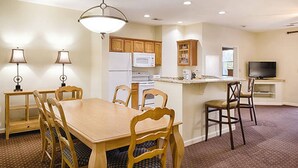 A compact kitchen with wooden cabinets, a microwave, and a refrigerator. There is a dining table with chairs and a small island with a sink. - 2BD/Williamsburg at Governor's Green - Lots to do! (Williamsburg)