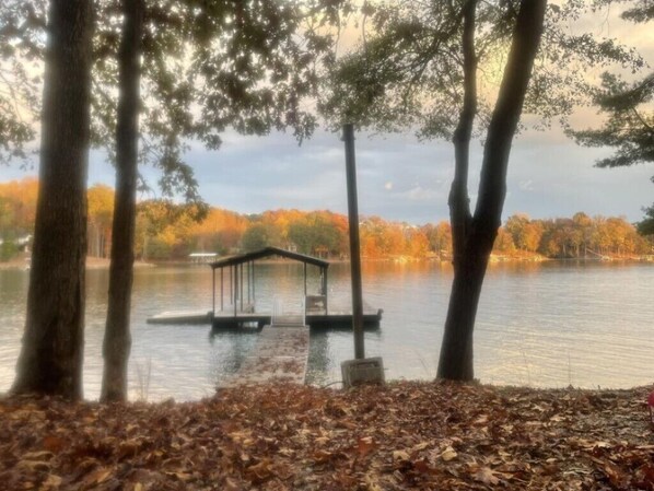 A tranquil lakeside scene with a wooden dock leading to a covered seating area.