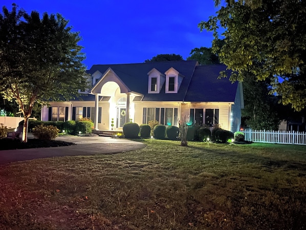 A two-story house with a front porch, a driveway, and a white picket fence.