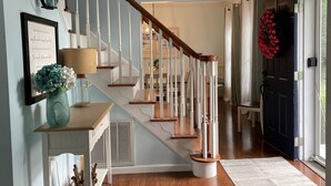A staircase with wooden steps and white railings, a chandelier, a framed quote, and a vase with flowers.