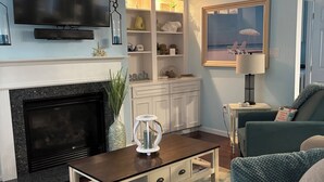 A living room with a fireplace, a television, a ceiling fan, and a bookshelf.