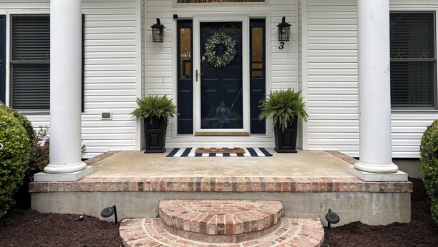 A house with a front porch, a black door, and two potted plants.