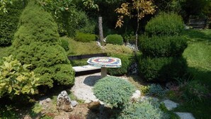 Un jardin avec une table en mosaïque circulaire, entourée de divers arbustes et plantes.