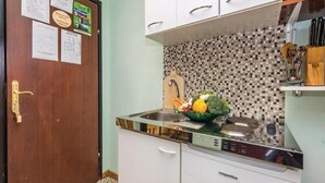 Une cuisine avec des meubles blancs, un pare-feu en carreaux et un espace près de l’évier où se trouve un panier rempli de fruits et de légumes.