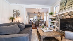 Een woonkamer met een grijze bank, een houten salontafel en een open haard met een stenen omlijsting.