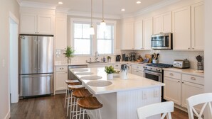 A modern kitchen with white cabinetry, a stainless steel refrigerator, a microwave, and a large island with bar stools. - Seabrook Farmhouse, Elk Creek | Hot Tub | Sleeps 10, Dog Friendly (Pacific Beach)
