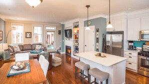 A modern kitchen with white cabinetry, a central island with stools, a built-in oven, and a stainless steel refrigerator. - Seabrook A Stones Throw | Pet Friendly, Hot Tub | 2BR, Sleeps 6, Downtown (Pacific Beach)